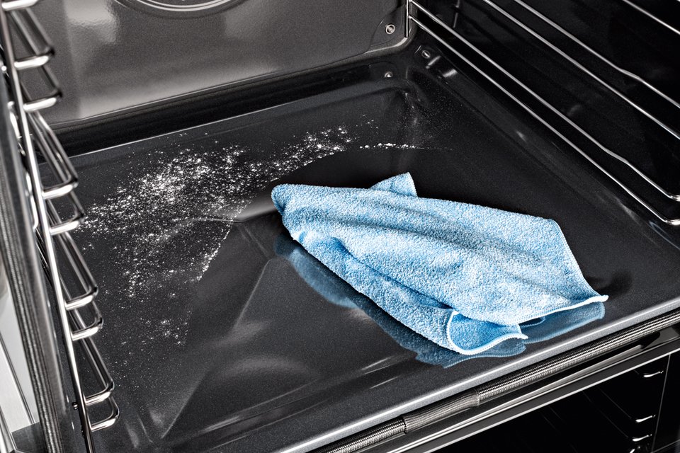 Inside of a Miele oven being cleaned with a blue cloth.